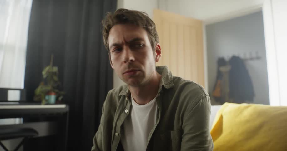 A man is sitting on the couch and he turns his head as he is startled by something and he stands up