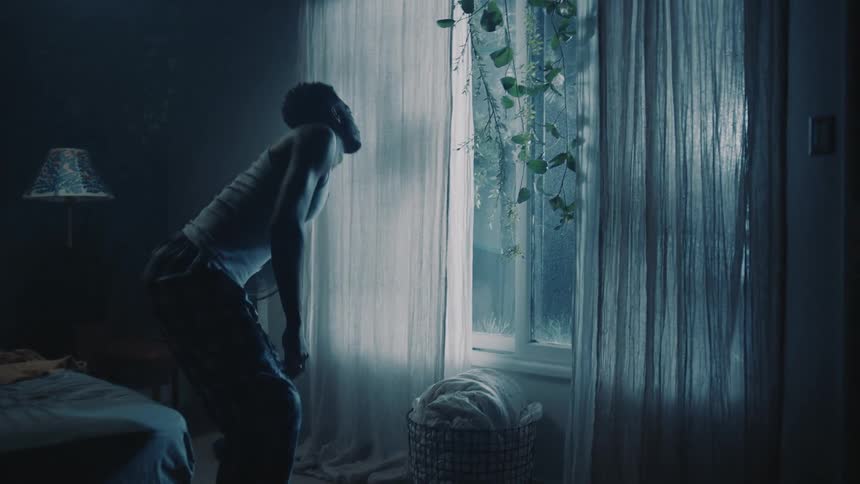 Man sitting on the bed stands up to open a window in the bedroomtion