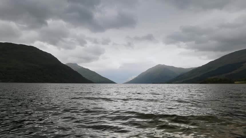 Light reflects on water was it ripples and sparkles under a cloudy sky with mountains in the distance