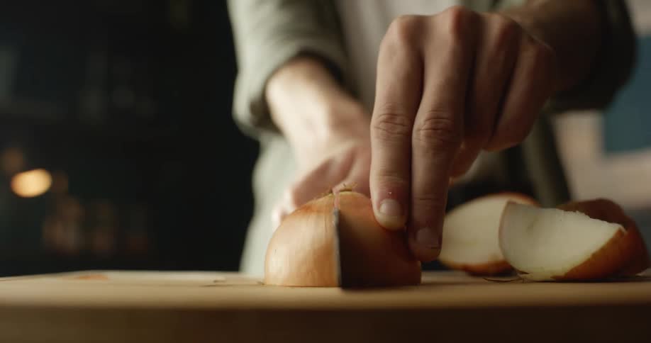 Close up of a woman cutting an onion over a table with a sharp kitchen knife