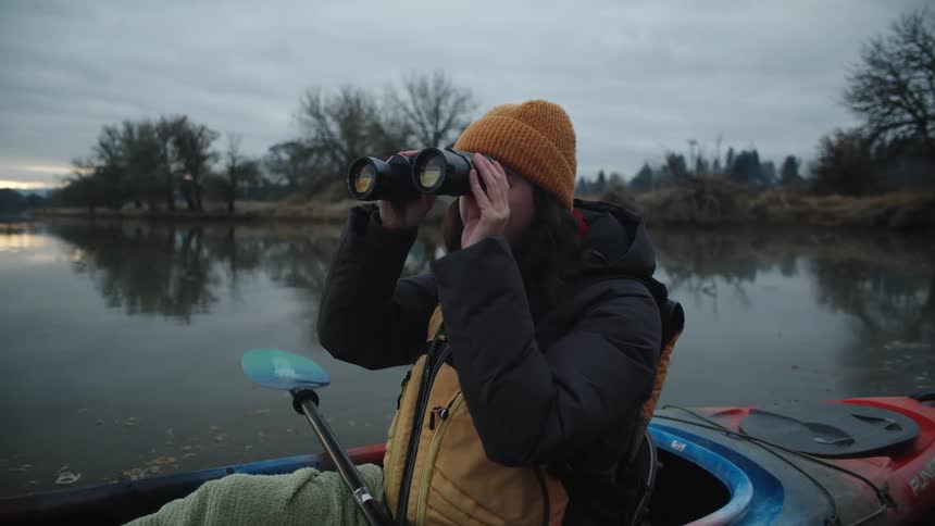 Woman sitting in a kayak on a lake looking through binoculars