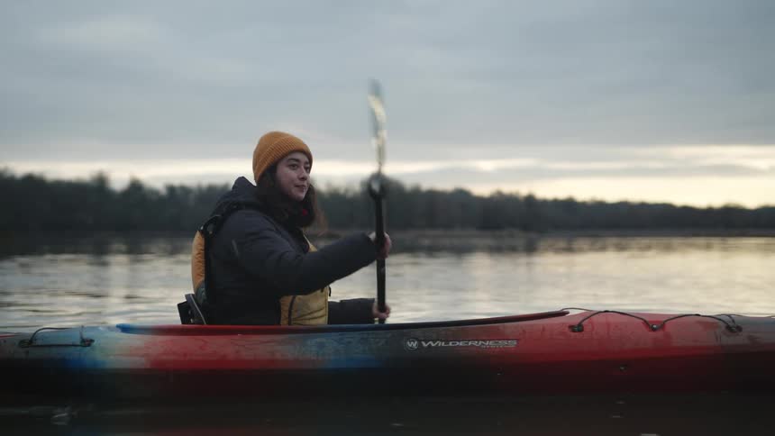 A woman is paddling in a kayak on a lake at sunset