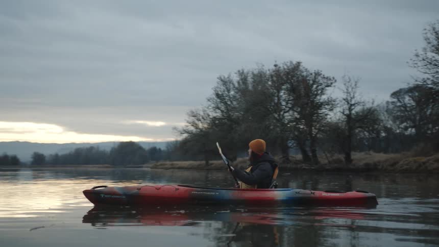 A young woman paddles across a lake in a kayak on a cloudy day