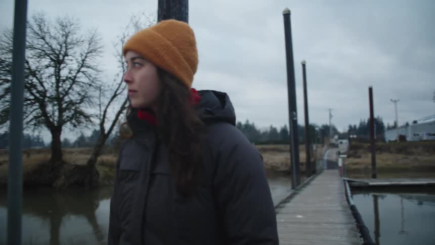 Woman wearing a parka walks on a pier next to a building in the lake