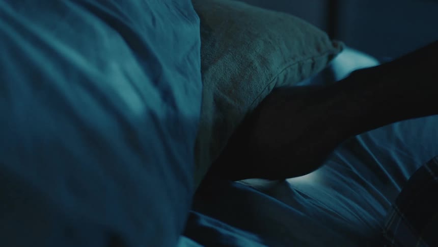 A person receives a smartphone from beneath a pillow on a bed