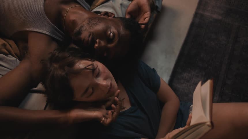 Man resting in the bed playfully teases his girlfriend reading a book