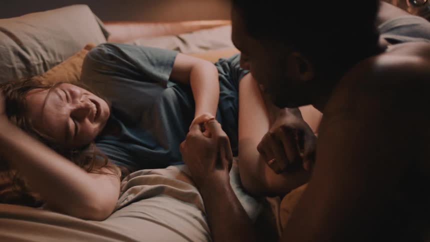 A man and woman are laughing as they are wrestling and playing on a bed