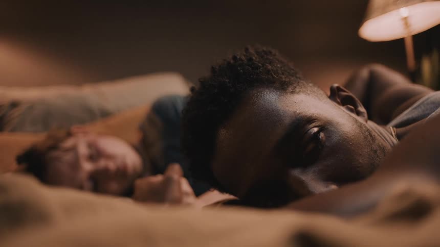A man sleeping in bed with a woman opens his eyes