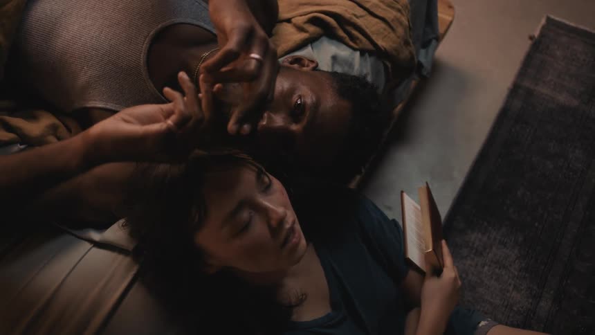 A man is stroking a womans hair with his fingers while she is reading a book