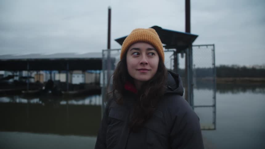 A young woman looks around at her surroundings while standing in a marina on a lake on a cloudy day