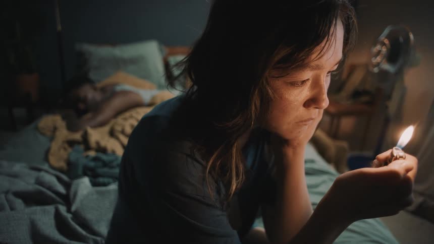 Young woman sitting on the corner of a bed turning a lighter on and off