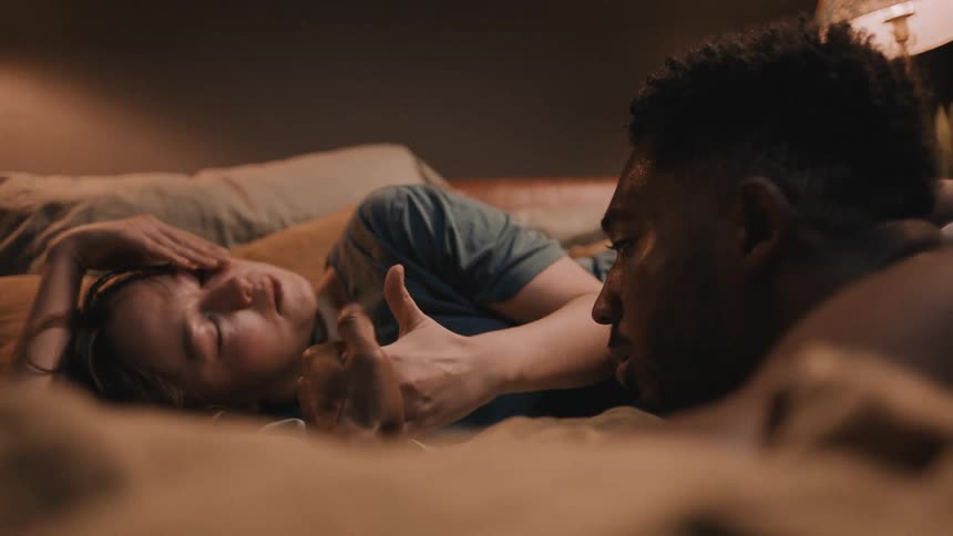 Relaxed couple talking in the bed while holding hands and playing with their thumbs