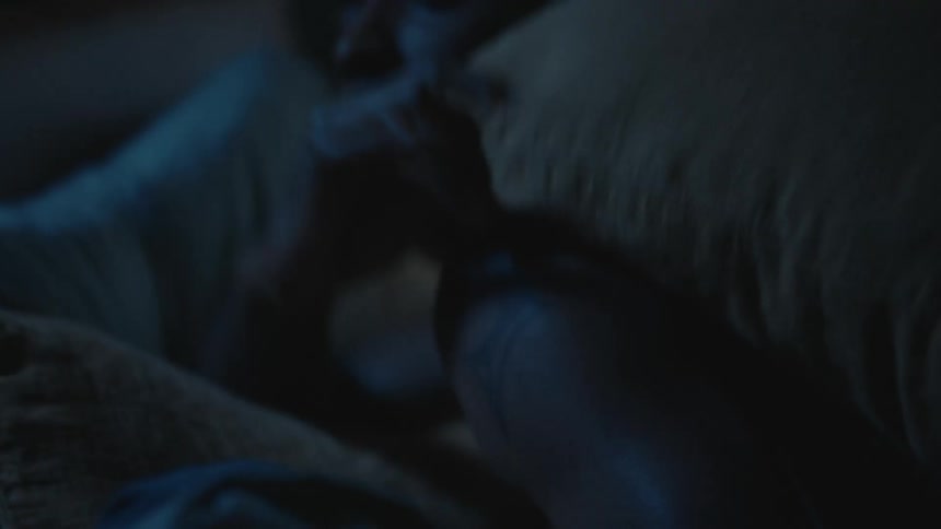Woman uses a pillow to hit softly her partner to stop using the smartphone in the bed