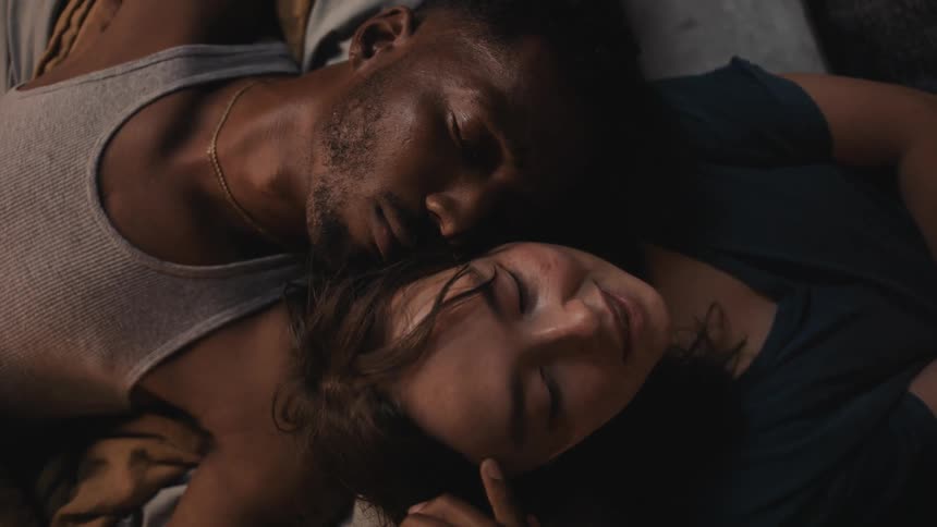 A man is caressing the face of a woman as she is reading a book out loud