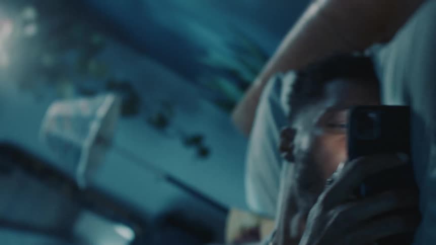 Man watches smartphone before lying down on bed then the other person in bed hits him with a pillow