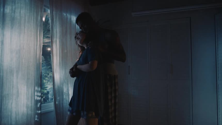 A couple slow dance by an open window at home