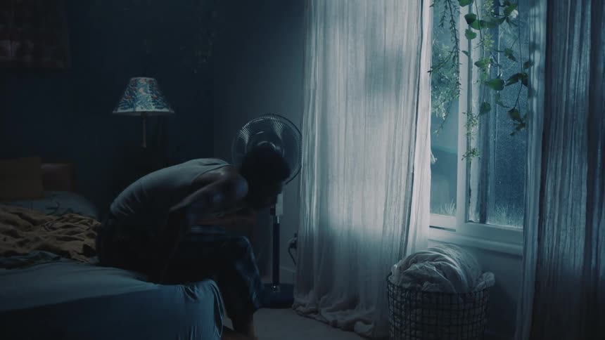 Man gets out of bed in dim room and closes window
