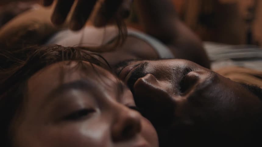 A woman is talking while a man laying next to her is caressing her face and hair