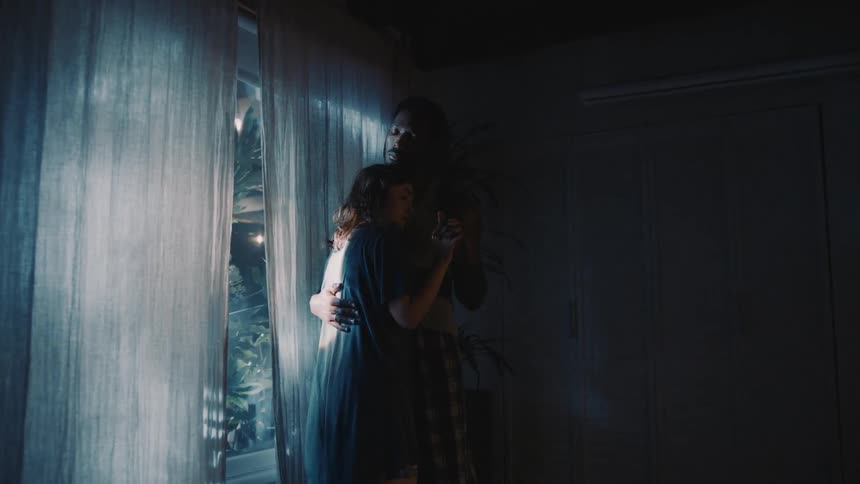 A couple slow dance next to a large window at home