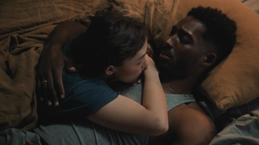 A man and woman are laying together in a bed and cuddling and talking