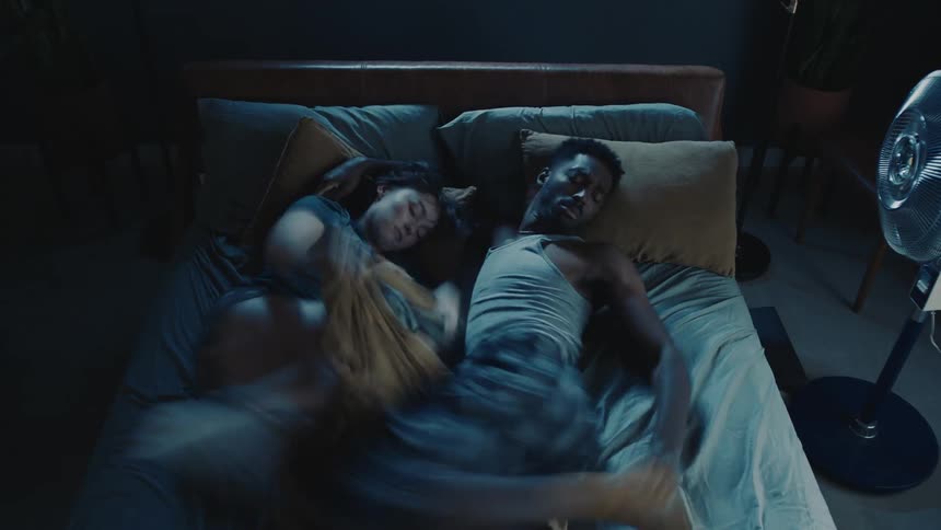 Couple sleeping in bed briefly pet cat as someone else adjusts sheet