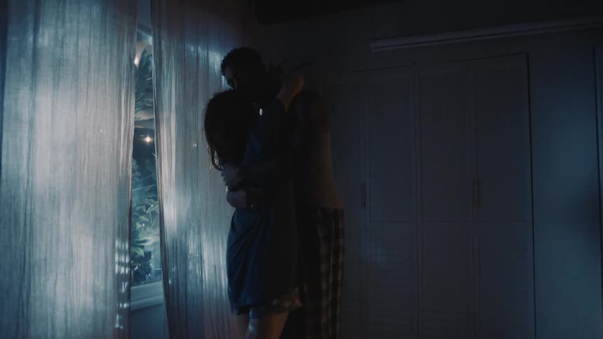 Couple slow dances in home near curtained window