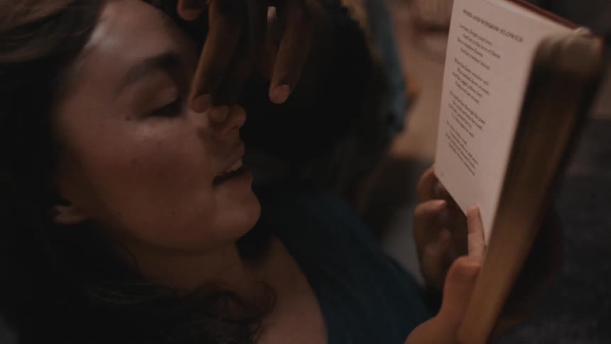 A man is stroking the face and nose of a woman while she is reading a book