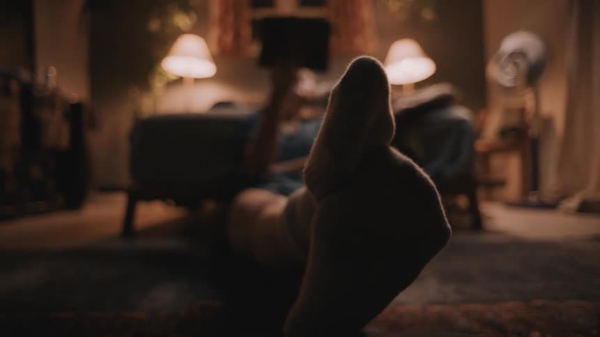 Person sits on the floor of a room wearing socks and moving their feet