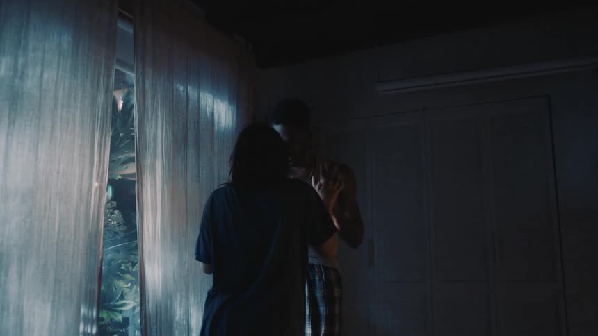 A man and a woman are standing inside their house near a window dancing together