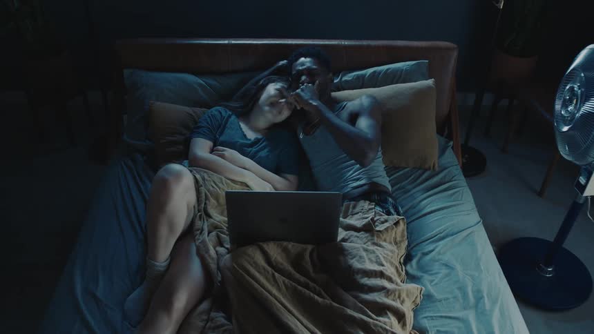 A man and woman laying in bed are tossing and turning then watching videos on a laptop before going back to sleep