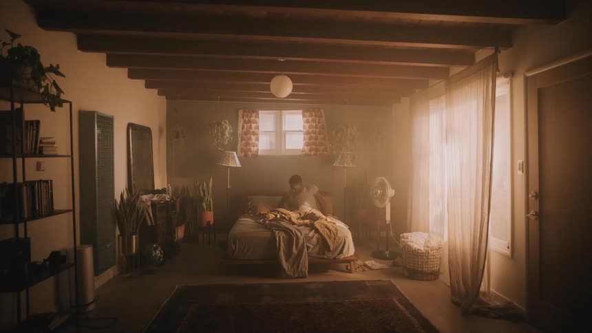A black male laying in bed in a messy bedroom