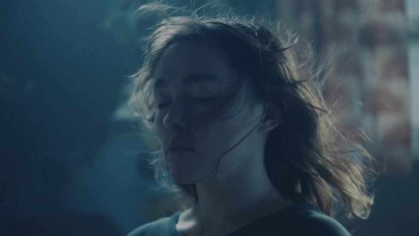 Woman stands near building at night with her eyes closed as wind ruffles her hair