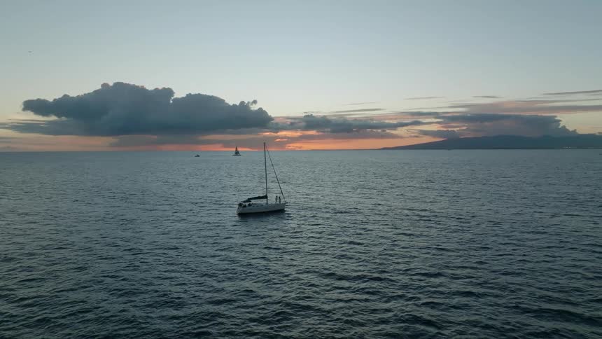 Aerial view of a couple standing on a sailboat in the ocean hugs at sunset