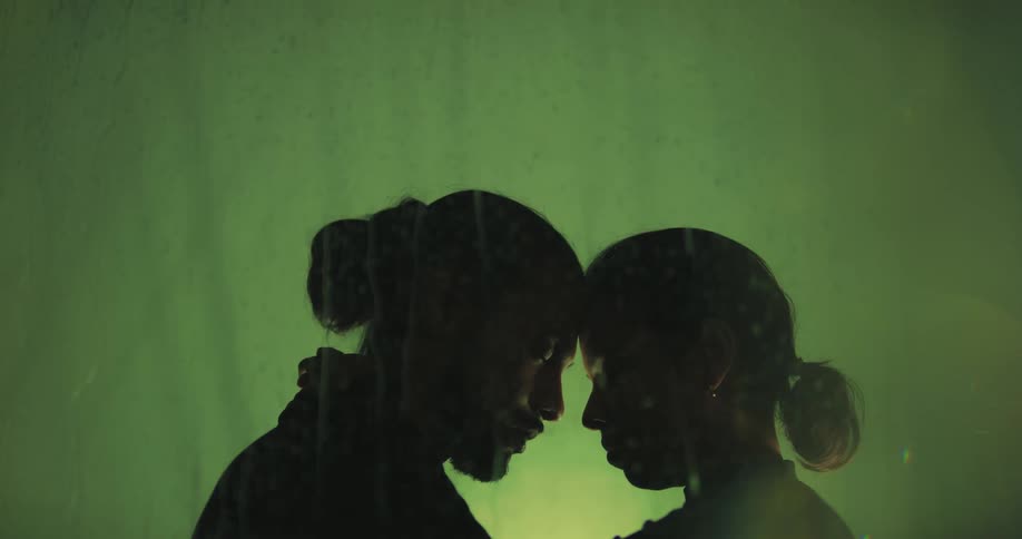 A man and woman stand in the rain with their heads pressed against one another