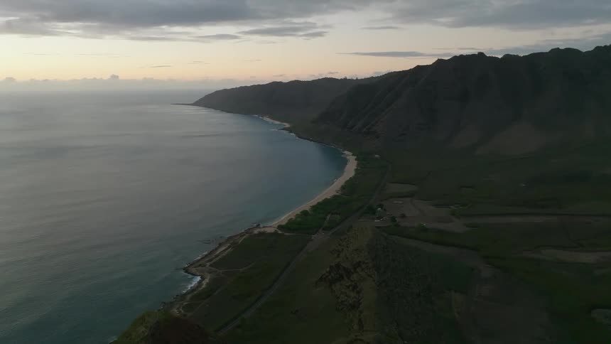 The sun is below the horizon as the waves crash onto a beach that is surrounded by cliffs