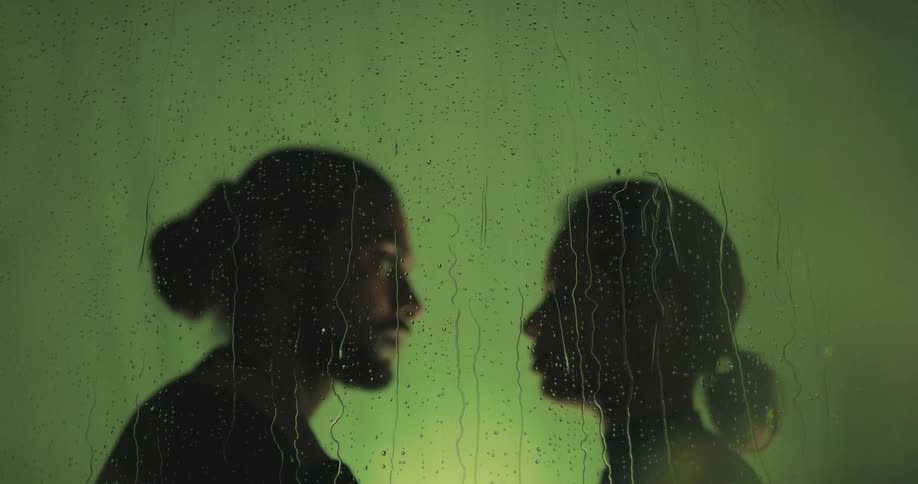 Man and woman look into each others eyes behind the windows while raining