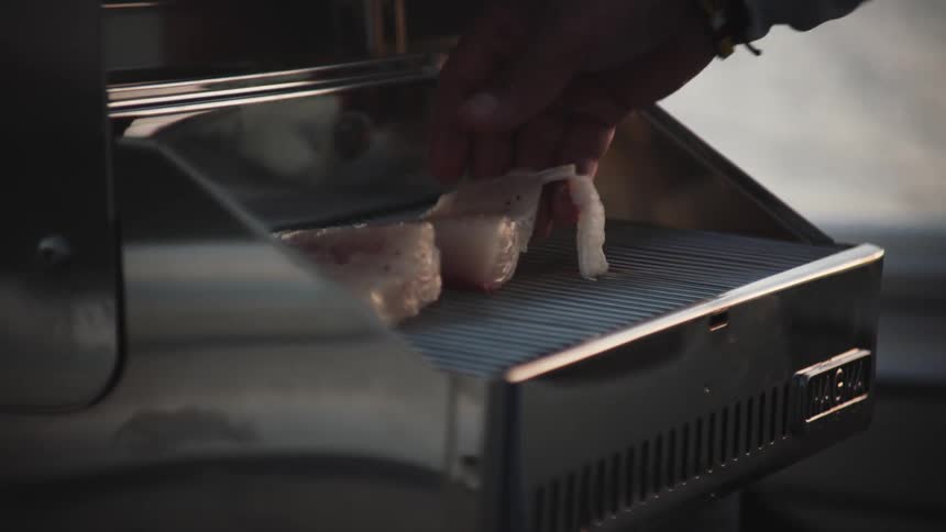 Man places raw fish fillets over a metallic grill