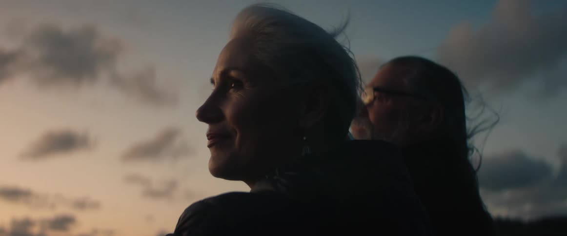 Wind blows through a couples long hair as they stand outside at dusk