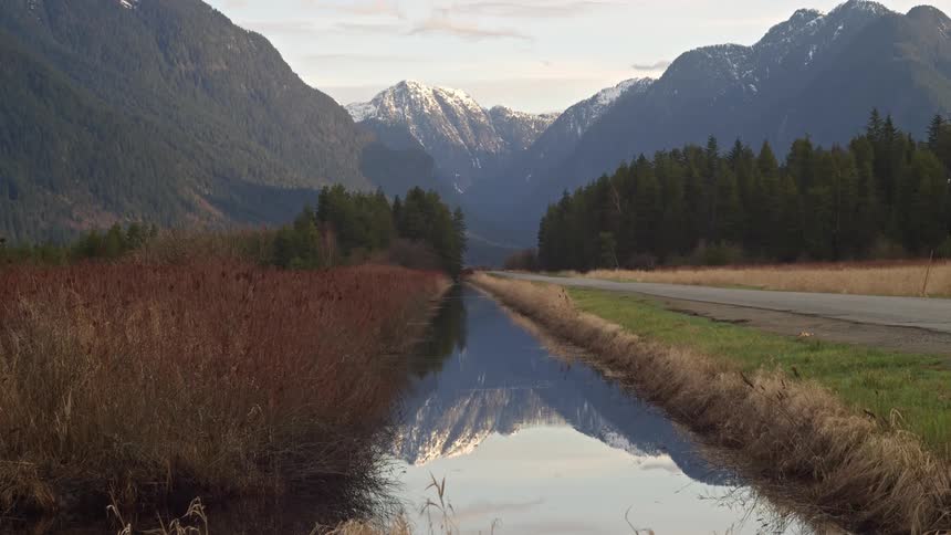 Calm stream flowing alongside a road in the countryside next to the mountains at morning