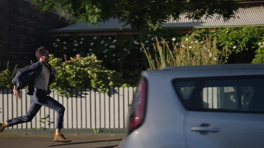 A man wearing a backpack runs down a sidewalk in a residential area during the day