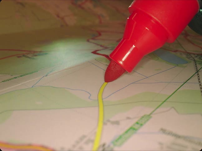 Someone traces over a line on a map with a pink marker