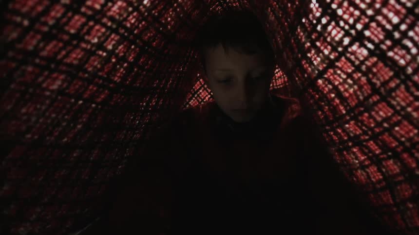 Boy sits in dark tent made with mesh sides