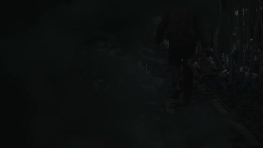 A man is walking through trees in a dark forest carrying a crate