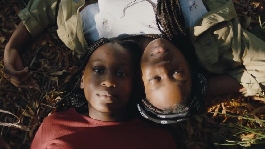 Two siblings lie on the ground with their heads touching