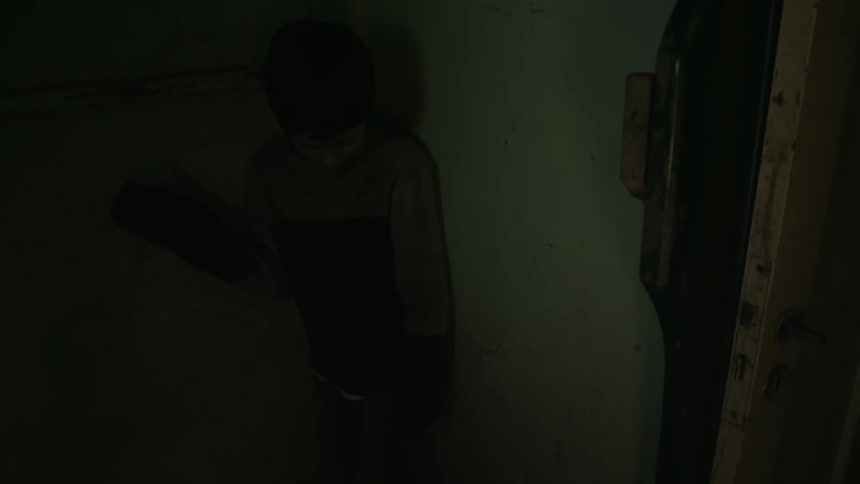 Angry adult pushes a young boy into the corner of a dark room at home