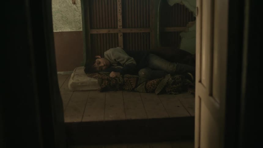 A boy rests in a dirty bed in a dilapidated building during the day