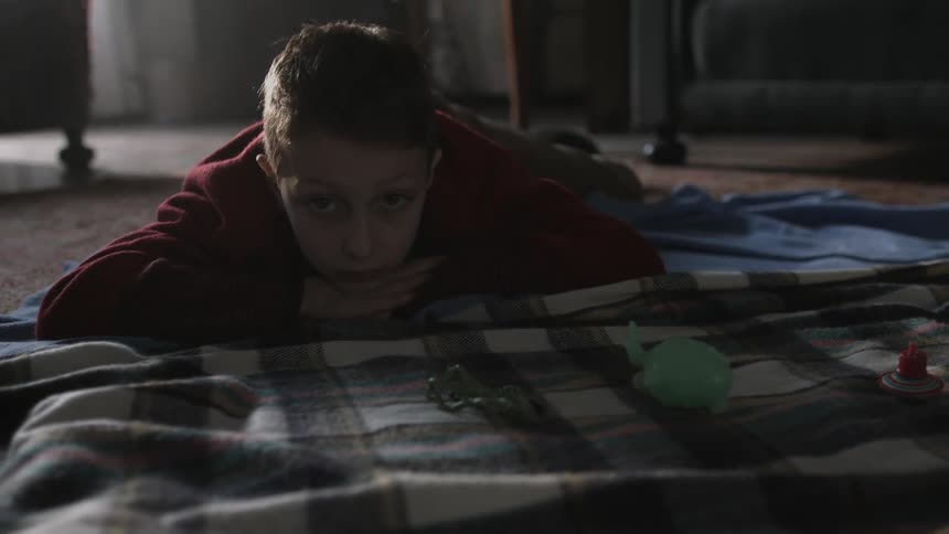 A boy is lying on the floor looking at his toys on a blanket