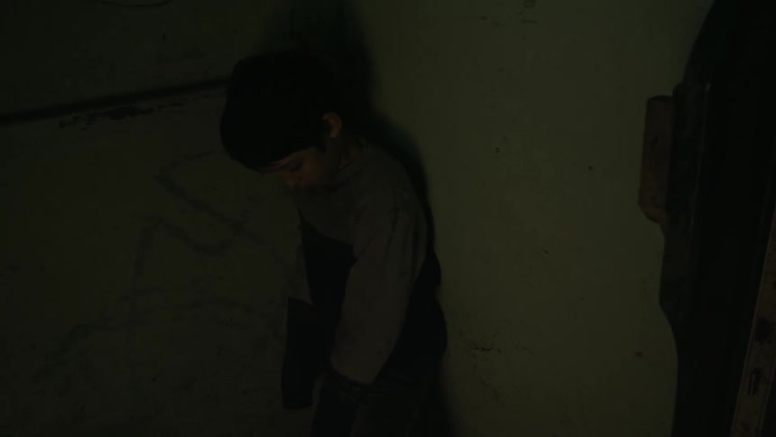 An adult walks in to a room and pushes a little boy in to a wall and the boy looks down at the ground as he is slumped against the wall