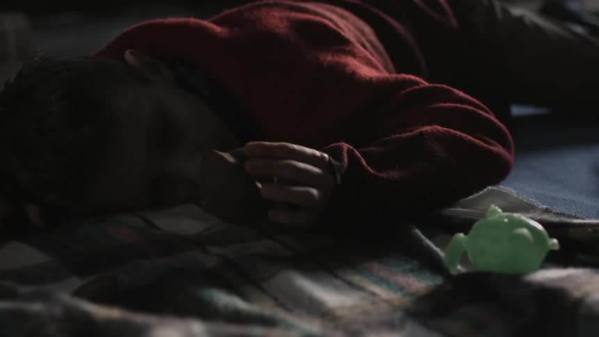 A sad looking boy lies on the floor and picks up a toy and looks at it and throws it back on the floor