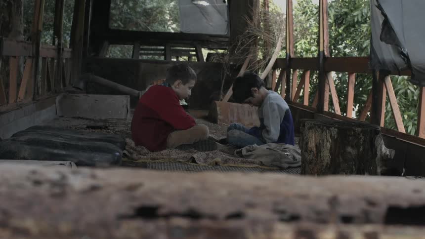 A sad boy with his head looking down at the ground sits in a treehouse with his friend and his friend pushes on his shoulder